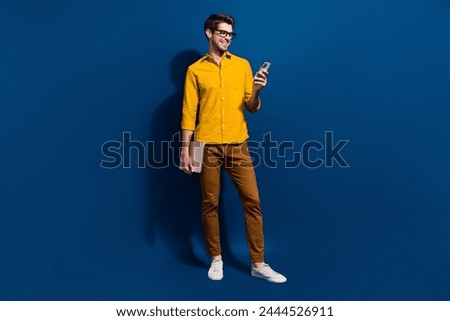 Full size photo of handsome young man hold netbook device smm manager dressed stylish yellow outfit isolated on dark blue color background