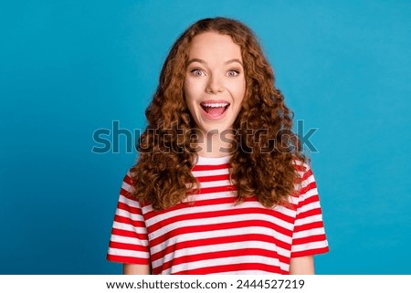 Photo of impressed overjoyed woman with wavy hairstyle dressed striped t-shirt astonished staring isolated on blue color background