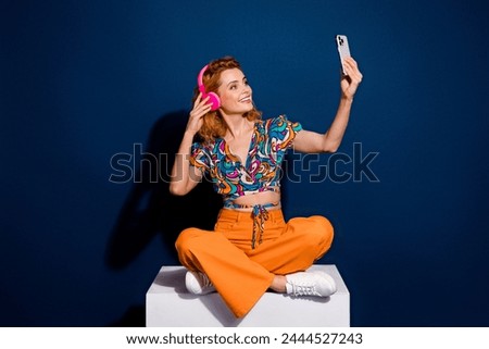 Full size photo of pretty young woman sit cube make selfie wear top isolated on dark blue color background