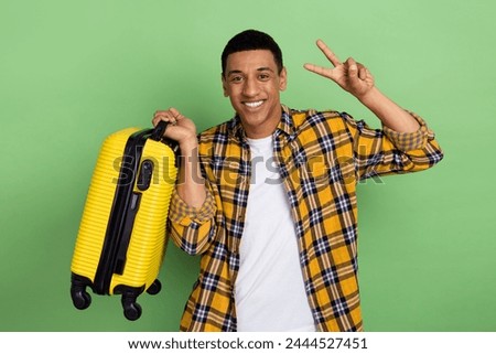Portrait of cheerful friendly person hold suitcase demonstrate v-sign isolated on green color background