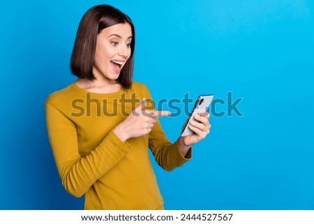 Photo of cheerful impressed woman wear shirt pointing finger modern gadget empty space isolated blue color background