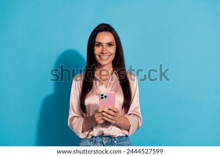 Photo of positive optimistic lovely girl with straight hairdo wear silk blouse holding smartphone isolated on blue color background