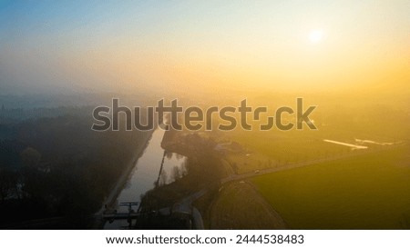 The break of day casts a golden hue over a meandering canal, with the gentle mist enhancing the tranquil rural ambiance. Sunrise over Canal with Soft Mist in the Countryside. High quality photo