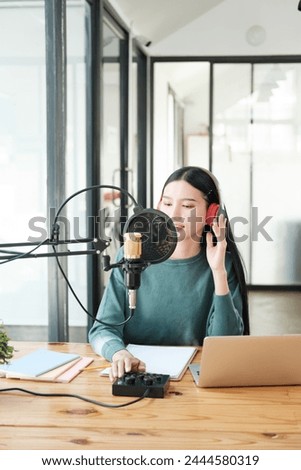 A woman is sitting at a desk with a microphone and a laptop. She is wearing headphones and she is recording a podcast or a voiceover. The room is well-lit and has a modern, professional feel