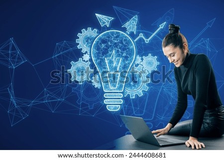 Attractive happy young businesswoman using laptop on desk with glowing blue lightbulb, cogwheel and arrow hologram on polygonal background. Innovation and creative idea concept