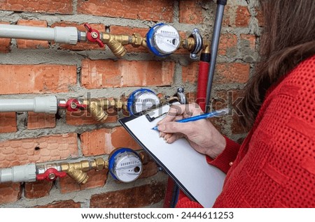 Woman checking the readout on a water meter. Water pipe system and water meters in building. Royalty-Free Stock Photo #2444611253
