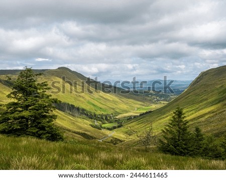 A wide view of the mountains and valleys in Ireland, with green grassy hills under grey clouds at Glengesh, County Donegal