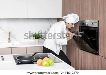Young inexperienced cooker trying to open the oven but something going wrong. Burnt food and bad smell concept Royalty-Free Stock Photo #2444619679