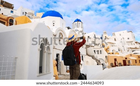 Young tourist man backpack using smartphone take picture at View of blue church dome in Oia village,Santorini,Greece
