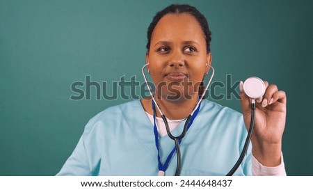 Black female doctor uses stethoscope to listen to heartbeat, in scrubs Royalty-Free Stock Photo #2444648437