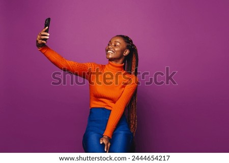 African woman with purple background. Smiling girl with two-tone braids taking selfie with smartphone. Casual and vibrant image of young female in Gen Z lifestyle.