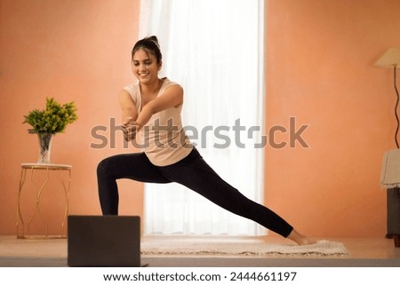 Young woman practicing yoga with online class through laptop