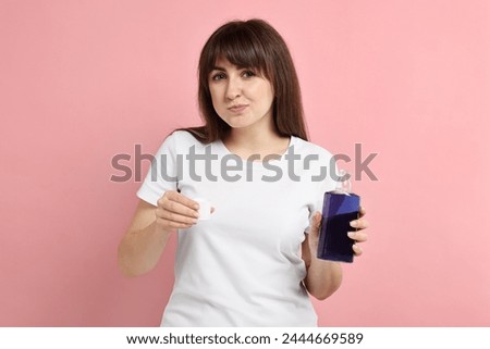 Young woman using mouthwash on pink background