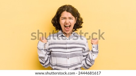 pretty hispanic woman shouting aggressively with an angry expression or with fists clenched celebrating success