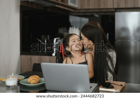 Loving young asian mother kissing little girl while working remotely at home