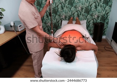 A serene red-lit room with a physiotherapist applying infrared heat therapy. Royalty-Free Stock Photo #2444686773
