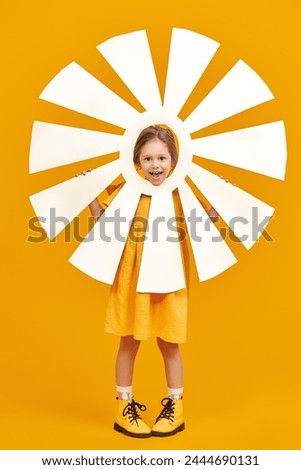 Full length portrait of a cheerful little girl in a yellow dress and yellow shoes, posing emotionally with a cardboard sun. Yellow studio background. Kid's fantasies and dreams. Summer Fashion.