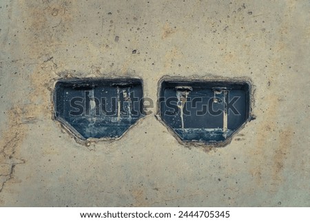 Black mounting box for electrical outlets in a light gray plastered wall. Scratched old wall in close-up. Abstract background. Architecture