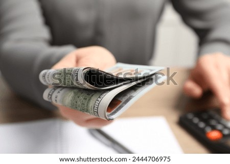 Money exchange. Woman holding dollar banknotes at wooden table, closeup