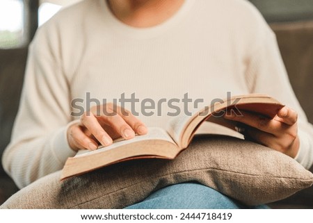 Asian woman sitting reading book on cozey couch sofa in living room with sun light morning. People stay home part time relax at home. Good time quality life rest calm happiness