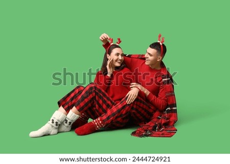 Happy young couple in Christmas pajamas and with plaid sitting against green background