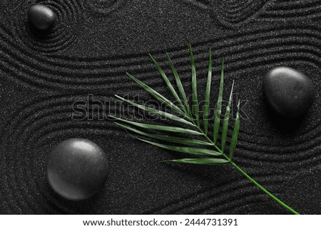 Spa stones on black sand with lines and palm leaf. Zen concept
