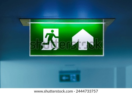 close-up green fire emergency exit sign on the ceiling showing the way to escape 