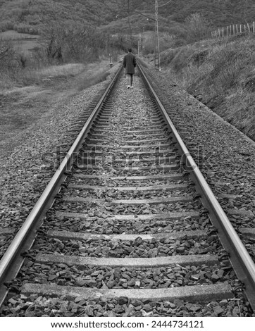 Black and white photograph of a person walking alone on train tracks