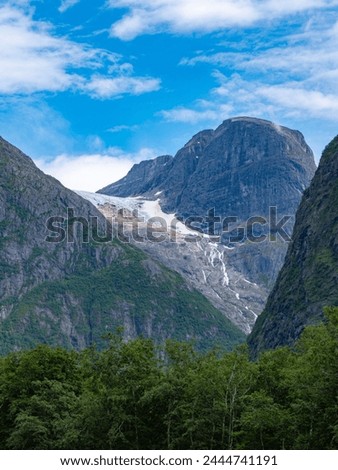 The Kjenndal Glacier is a branch of the Jostedalsbreen. It is located south of the Lovatnet near Loen, Bodal, Stryn. Beautiful mountain peaks. In the foreground you can see the green treetops.
