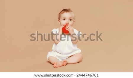 Portrait of cute baby holding red apple fruit sitting on the floor on brown studio background