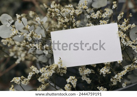 Floral wedding, birthday mockup. Blank textured paper business card, invitation. Limonium flowers and eucalyptus tree branches bouquet in metal bucket. Blurred background, floristry concept. Top