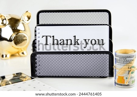 Text Thank You on a white notepad with money and a piggy bank in the background out of focus