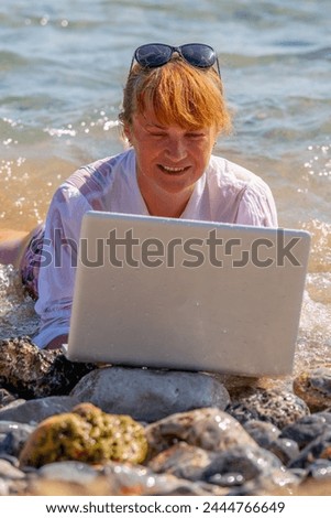 Happy business woman working anywhere and anytime. She working online with laptop on the beach of sea or ocean. Vertical image.