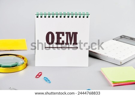 OEM original equipment manufacturer concept. Text on a white notepad on a gray background next to office supplies