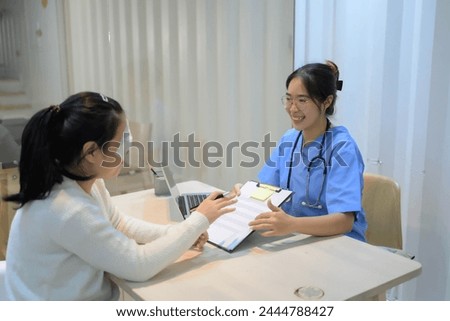 A woman is sitting at a desk with a clipboard in front of her. The woman is smiling and the nurse is smiling back