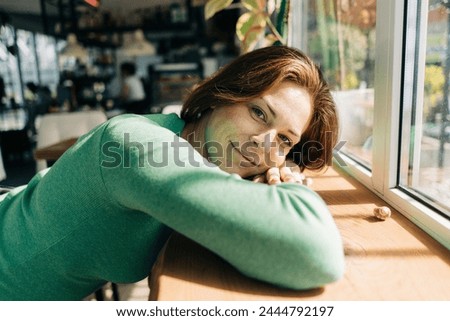 A woman lies leaning on a window sill in a cafe illuminated by the sun's rays. Royalty-Free Stock Photo #2444792197