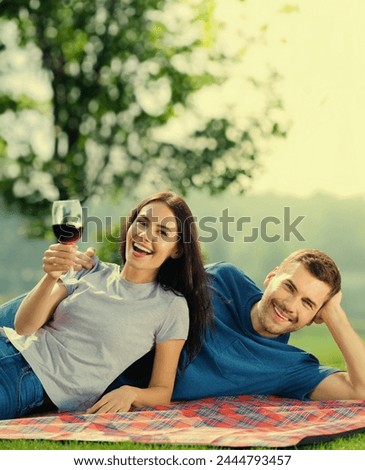Sunny image of excited young attractive amorous couple in love, lay together on picnic blanket, with red wine. Cheerful smiling man and woman outdoors. Happy summer time.