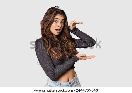 Young Caucasian woman in studio setting shocked and amazed holding a copy space between hands.