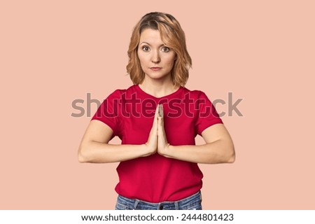 Blonde middle-aged Caucasian woman in studio praying, showing devotion, religious person looking for divine inspiration.