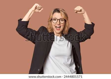 Caucasian woman in black business suit showing strength gesture with arms, symbol of feminine power