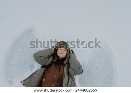 positive emotional portrait of a beautiful smiling woman lying on the snow and posing for a photo