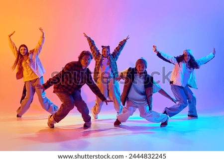 Dynamic image of young people, men and women in casual clothes dancing contemp against gradient studio background in neon light. Concept of modern dance style, hobby, active lifestyle, youth culture Royalty-Free Stock Photo #2444832245