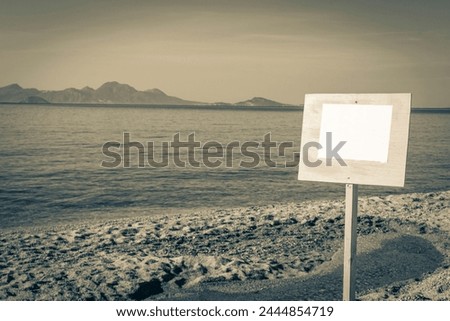 Old black and white picture of a blank information board sign at the the beautiful beach on Kos Island in Greece with panorama view on hills and islands.