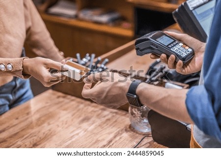Male barista waiter barman manager administrator holding credit card reader machine with female customer credit card for payment. Cropped shot of woman visitor client paying bank card for the purchase