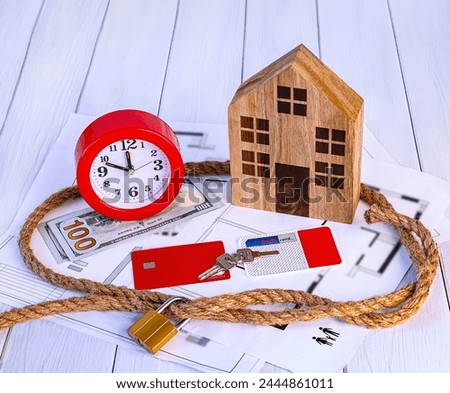 Home loan concept. Wooden house, rope knot, red alarm clock, house keys, dollar bills, credit cards on white background.