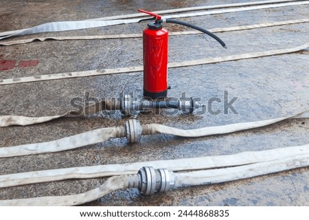 Red fire extinguisher cylinder with unwound fire hoses. Royalty-Free Stock Photo #2444868835