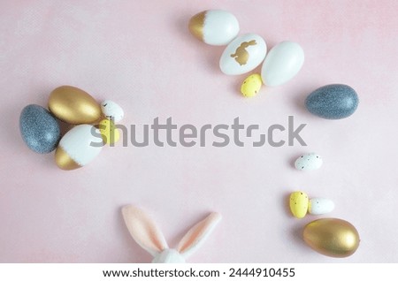 Easter eggs are yellow, dark blue, white and gold. Pink background. Easter. Bunny ears.