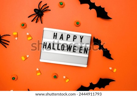 Traditional Halloween decor and candies on orange background with Happy Halloween on the lightbox