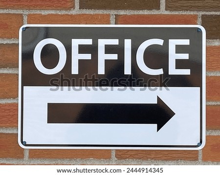 Posted OFFICE sign with a black arrow showing direction of the office on red brick wall