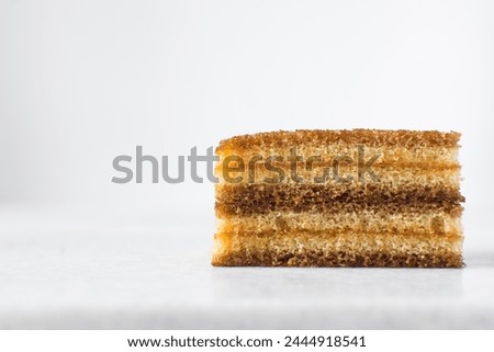 slice of vanilla cake with jam filling, thin layers of vanilla and chocolate cake with jam filling on a white background Royalty-Free Stock Photo #2444918541